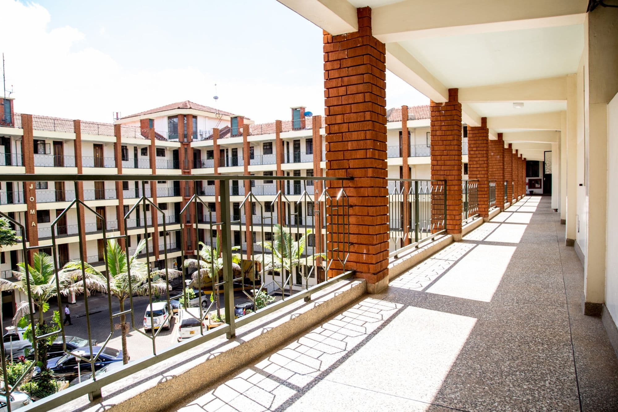 A sunlit open corridor with brick pillars overlooking the courtyard